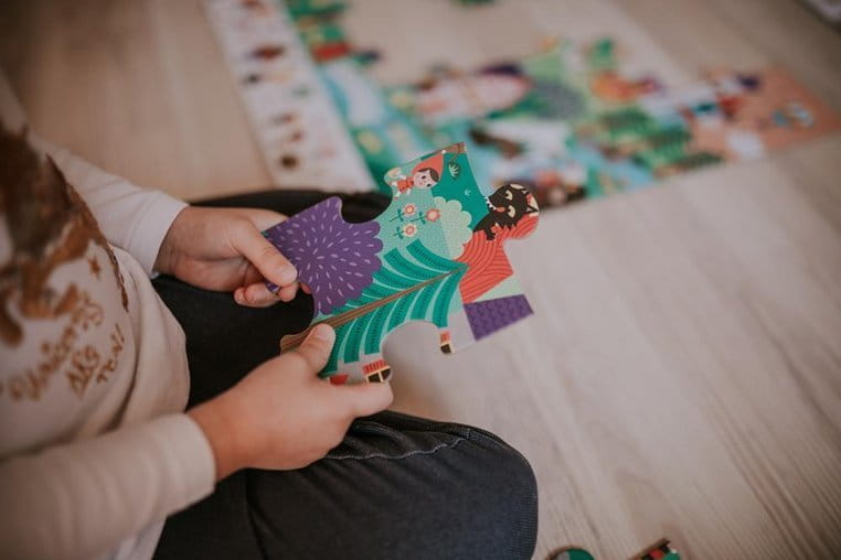 Dziewczynka siedzi na podłodze i trzyma w rękach puzzel