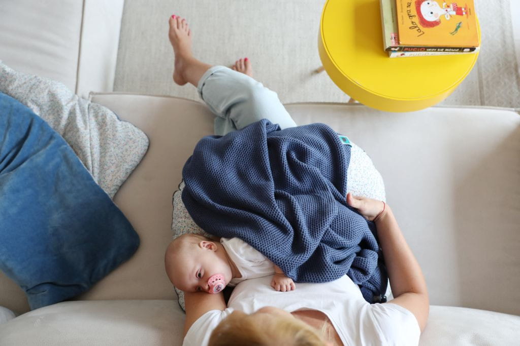 Mama trzyma dziecko na kolanach. Dziecko jest przykryte niebieskim kocem
