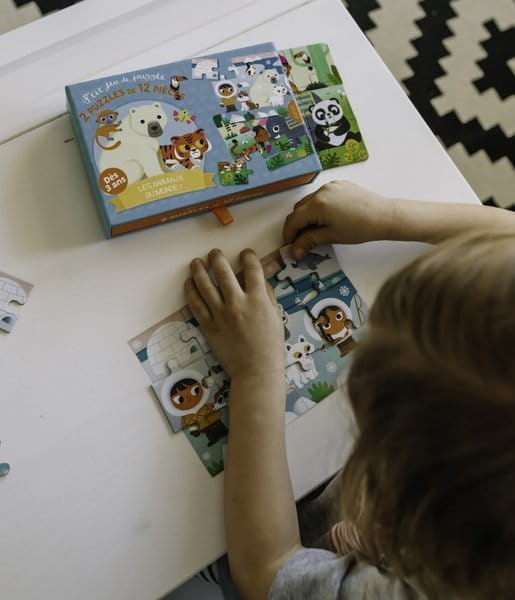 Dziecko siedzi przy stole i układa puzzle - widać fragment obrazka i dłonie