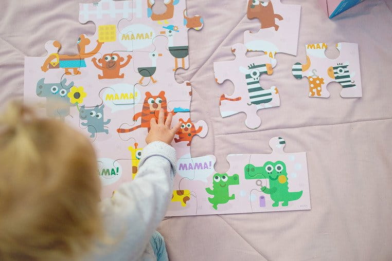 Dziewczynka siedzi na kocyku i układa puzzle z wizerunkami zwierzaków